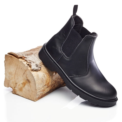 Black Chelsea boot leaning against a wooden log on a white background